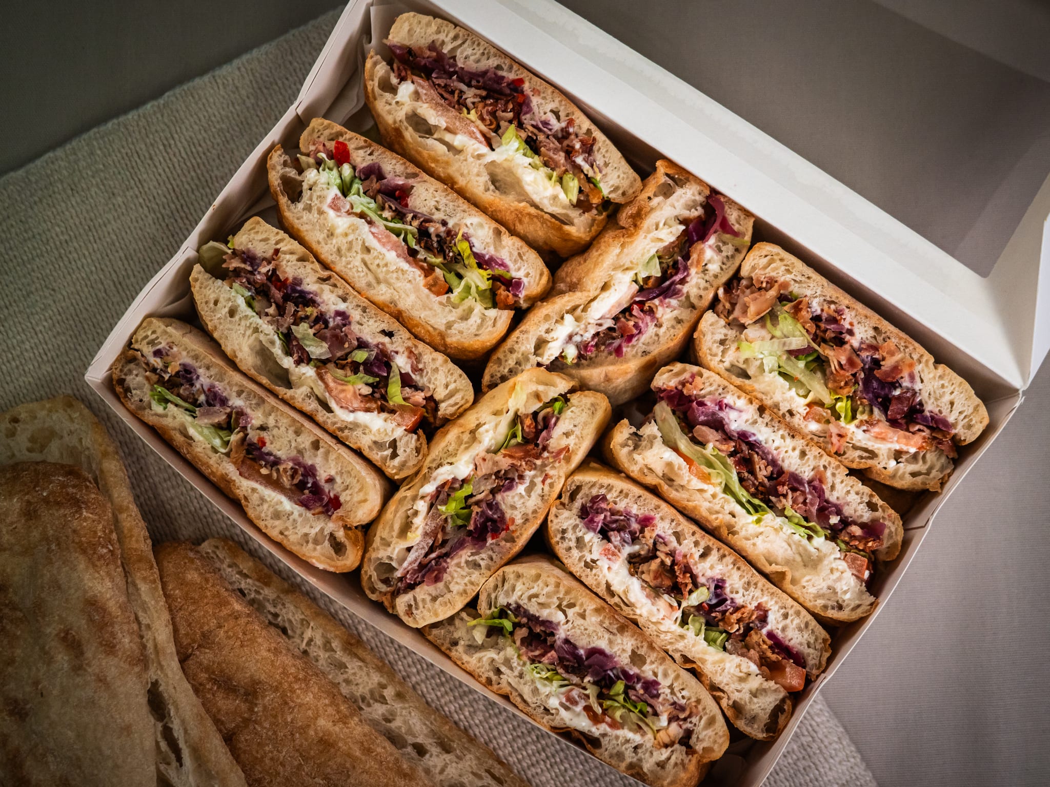 The Sub Side Blazin' Honey BLT features six halved sandwiches with lettuce, shredded cabbage, deli meat, and mayo. Two extra bread pieces are served on the side.