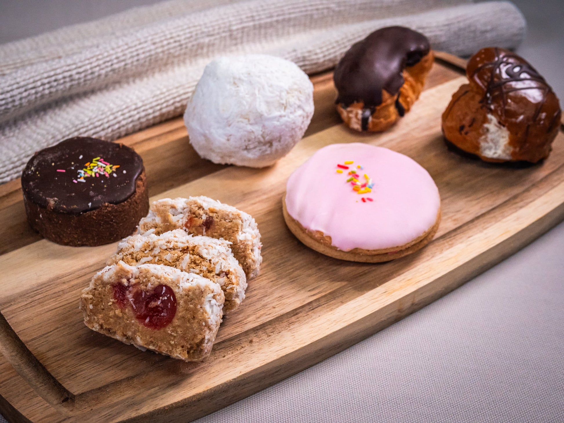 The Baker’s Box (15 pieces) by Sub Side features assorted pastries like chocolate tart, coconut slice, jam-filled slice, iced donut, Rolo Traybake, chocolate eclairs, and a powdered sugar-coated pastry.