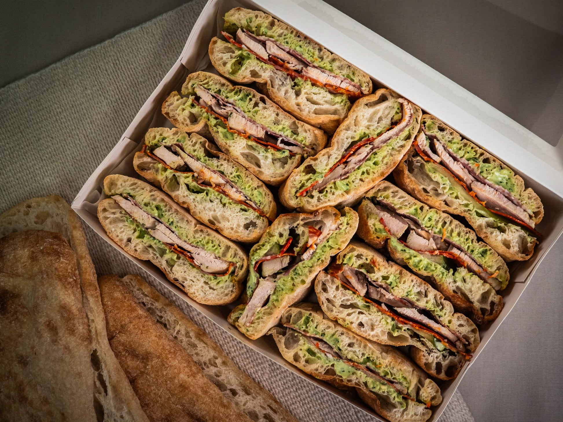 The Sub Side Mixed Sub Platter - 2 Full Boxes (serves 10) features neatly arranged ciabatta sandwich halves with grilled meat, lettuce, and red peppers, plus extra bread—ideal for sharing our signature subs at any gathering.