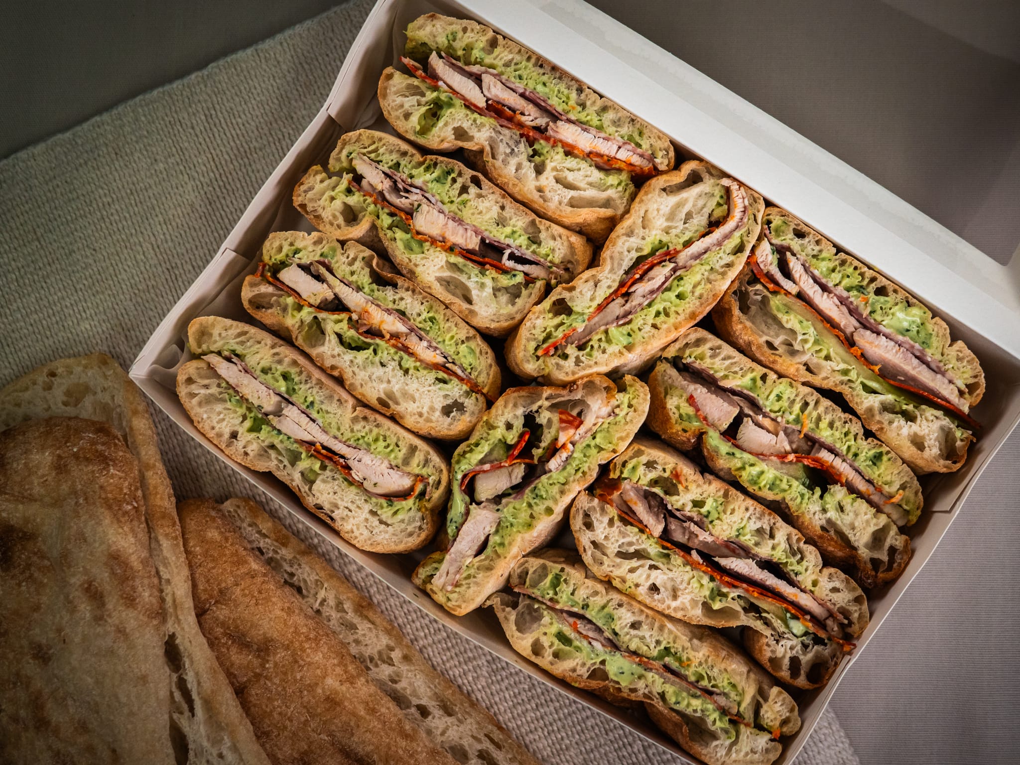 The Sub Side Mixed Sub Platter - 2 Full Boxes (serves 10) features neatly arranged ciabatta sandwich halves with grilled meat, lettuce, and red peppers, plus extra bread—ideal for sharing our signature subs at any gathering.