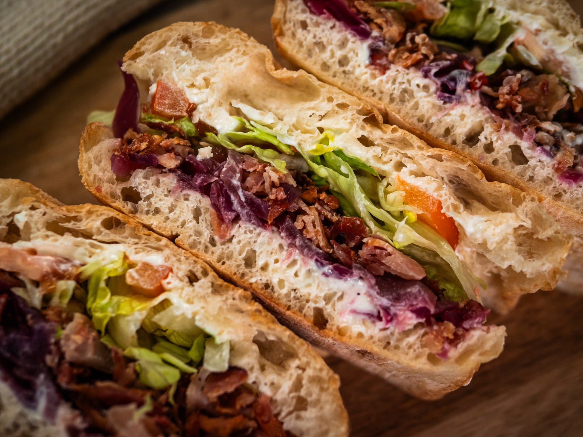 Close-up of Sub Side's Blazin' Honey BLT sandwiches, stacked with lettuce, tomato, bacon, creamy mayo, and hot honey red onions on rustic bread.