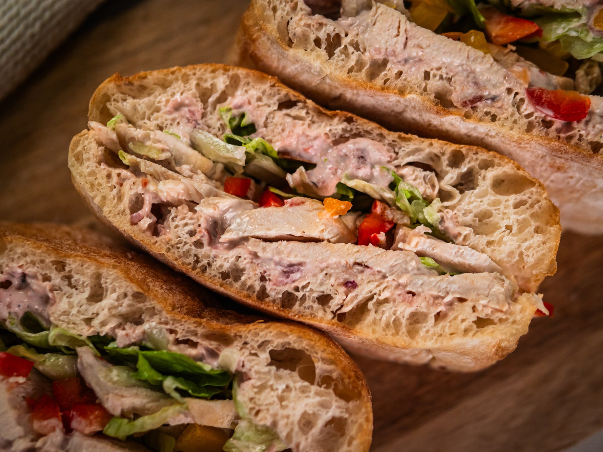 Close-up of Sub Side’s Roasted Chicken Crunch: sliced chicken breast, lettuce, mixed peppers, and hot red onion mayo on rustic bread, served on a wooden surface.