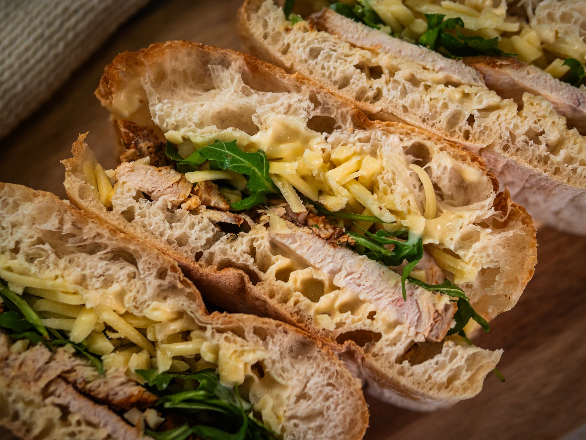 Close-up of Zaátar Zing by Sub Side: a chicken sub with crusty bread, Moroccan-spiced chicken, shredded cheese, arugula, creamy sauce, and fragrant Za’atar herbs.