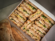 A box of Sub Side's Zaátar Zing ciabatta sandwiches with Moroccan-spiced chicken, cheese, and greens, plus extra ciabatta bread on the side.