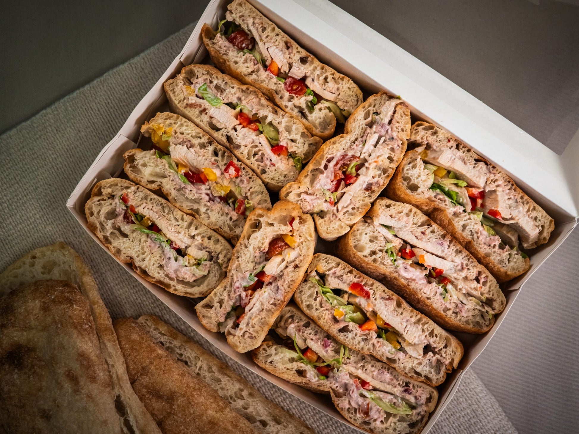 The Sub Side Mixed Sub Platter - 2 Full Boxes (serves 10) features assorted signature and vegetarian subs on whole grain bread, with extra bread slices included beside the party platter.