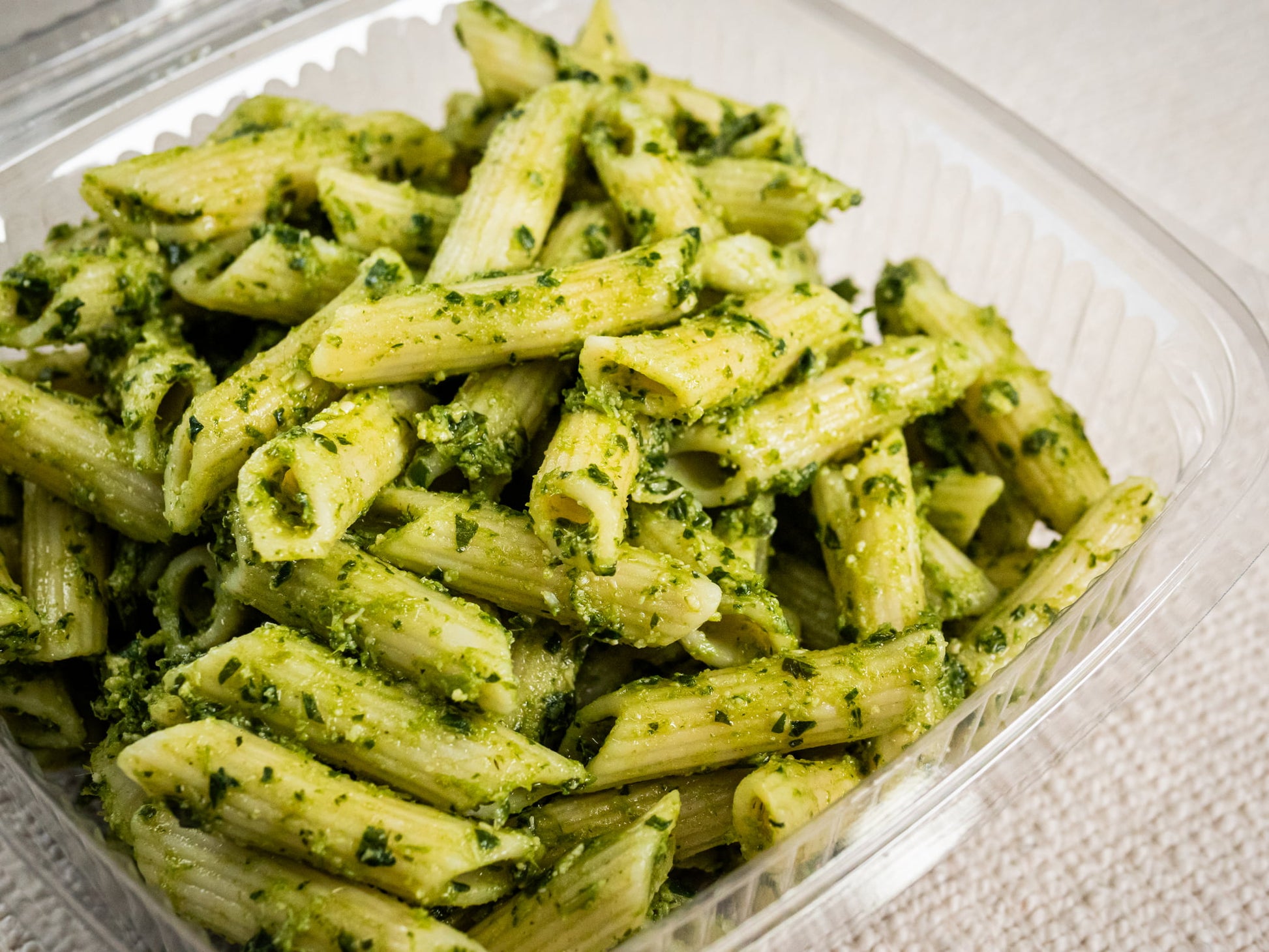 Sub Side Nut Free Pesto Pasta (500g) features penne coated in basil pesto with a touch of lemon, served in a clear plastic takeout container on a light surface.
