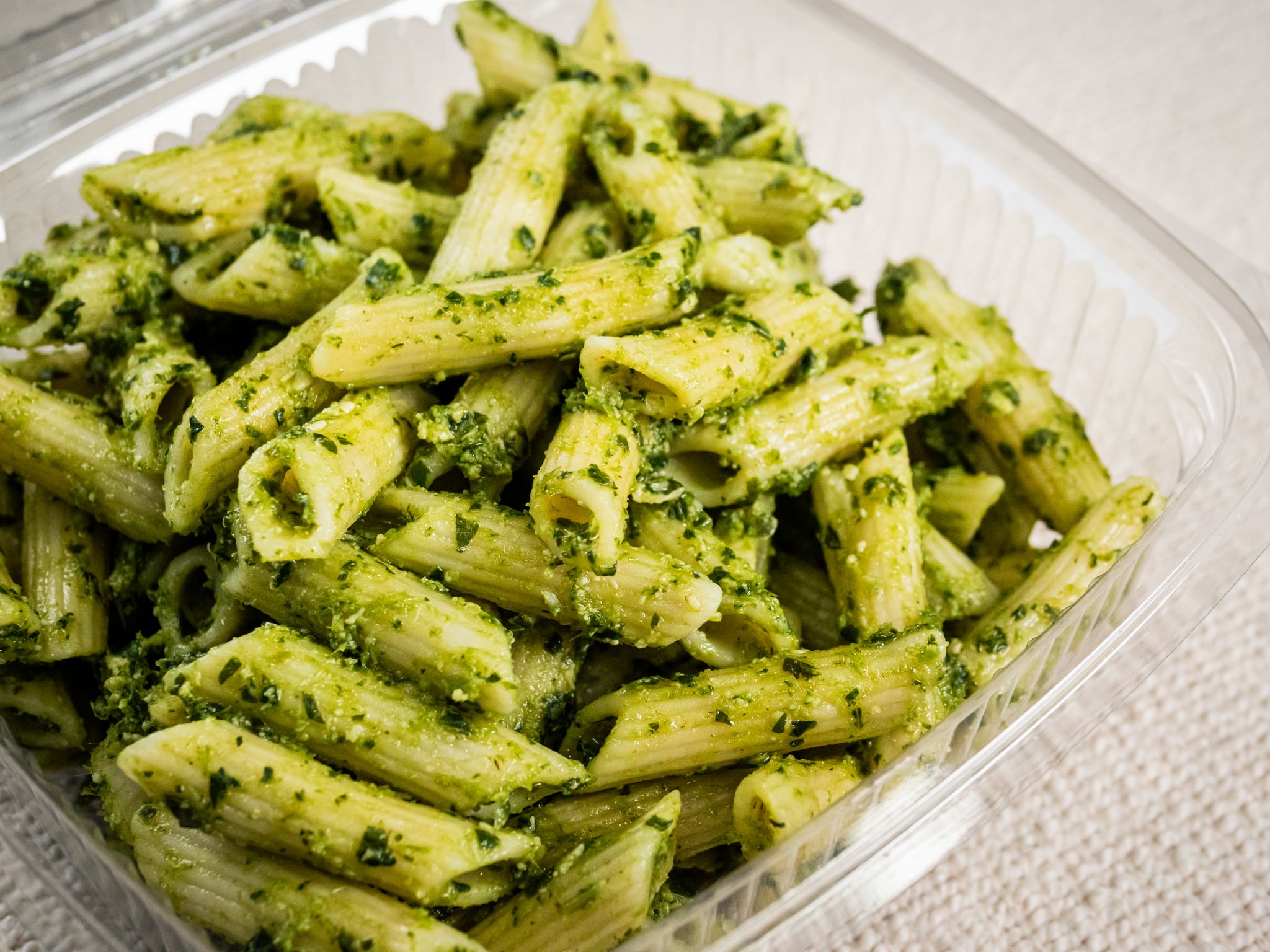 Sub Side Nut Free Pesto Pasta (500g) features penne coated in basil pesto with a touch of lemon, served in a clear plastic takeout container on a light surface.
