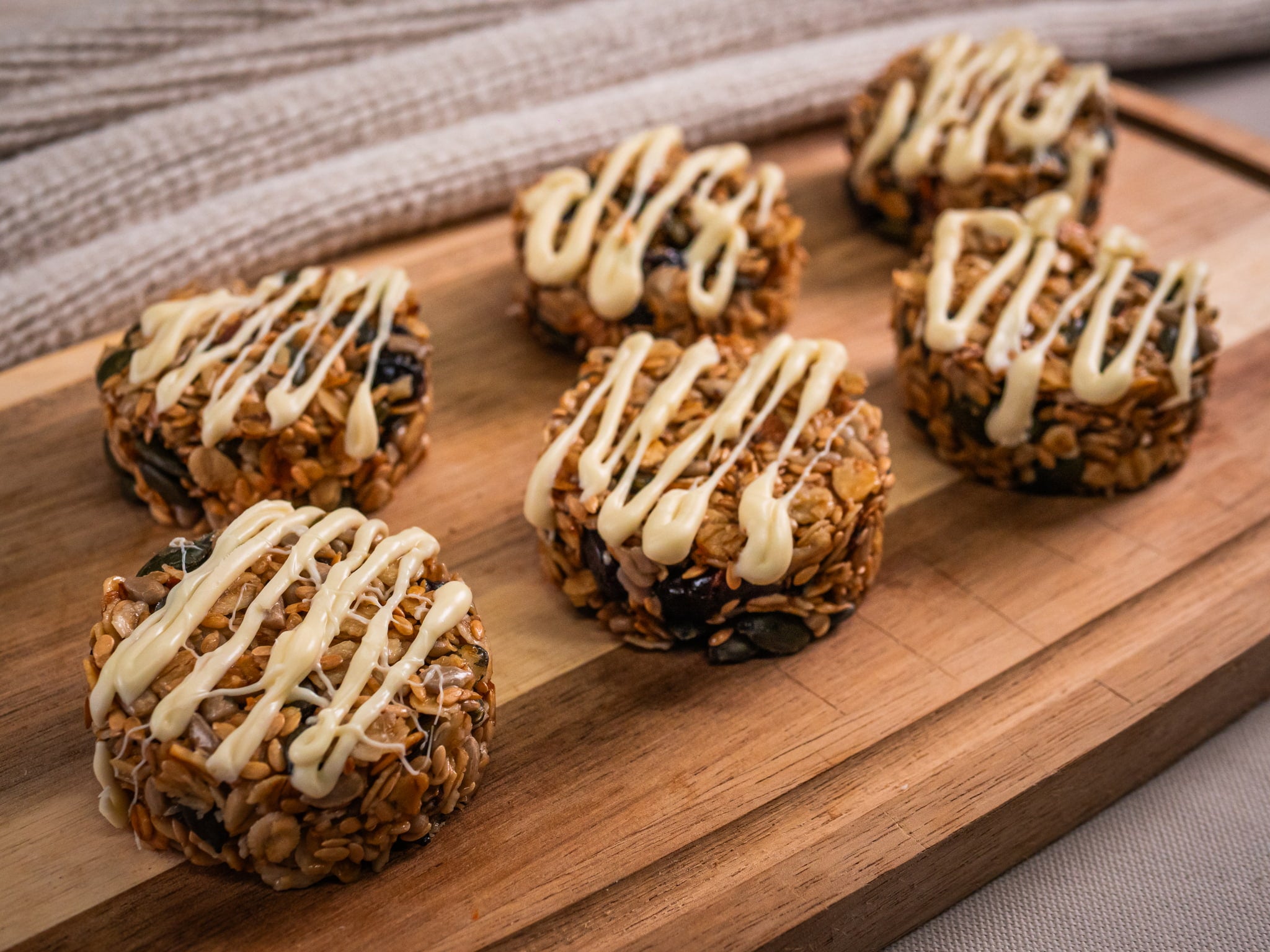 Six Sub Side Granola Bites White Chocolate (6 Pieces), made with seeds and dried cranberries and topped with white chocolate drizzle, are arranged on a wooden cutting board.