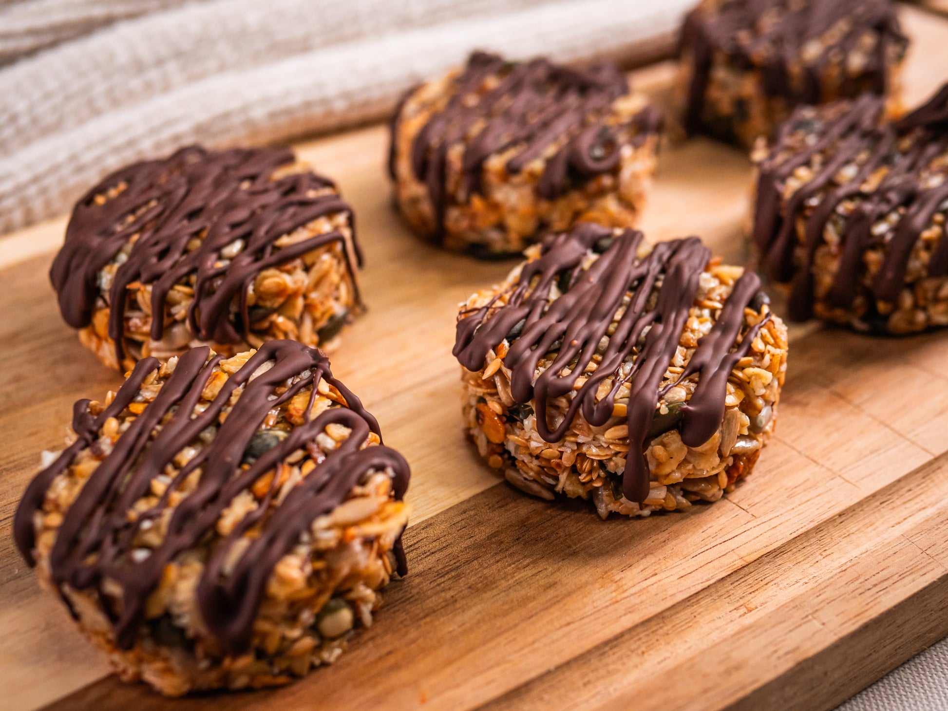 Sub Side Granola Bites Dark Chocolate (6 Pieces) are round oat clusters topped with drizzled dark chocolate, arranged on a wooden board for a delicious natural energy boost.