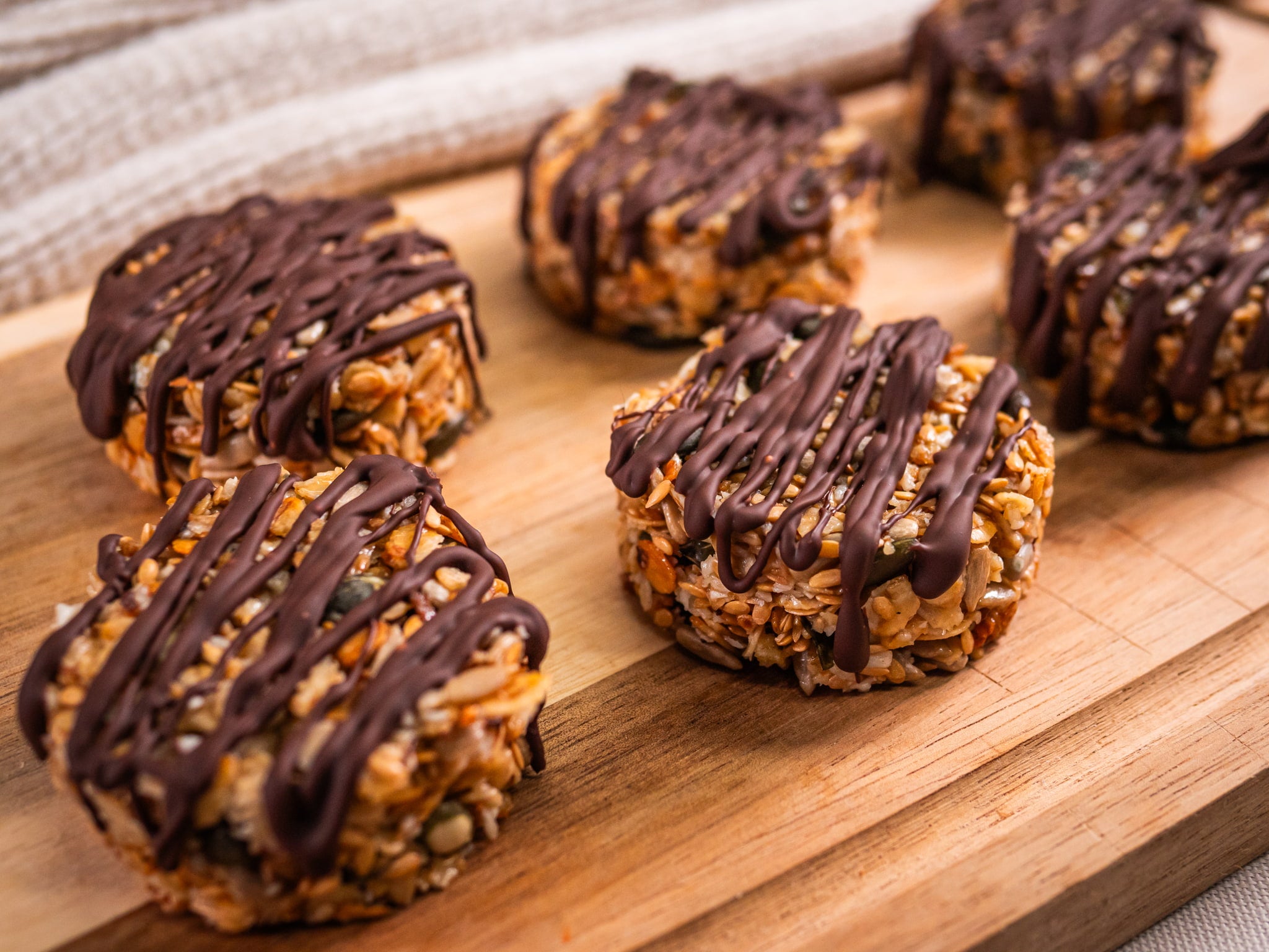 Sub Side Granola Bites Dark Chocolate (6 Pieces) are round oat clusters topped with drizzled dark chocolate, arranged on a wooden board for a delicious natural energy boost.