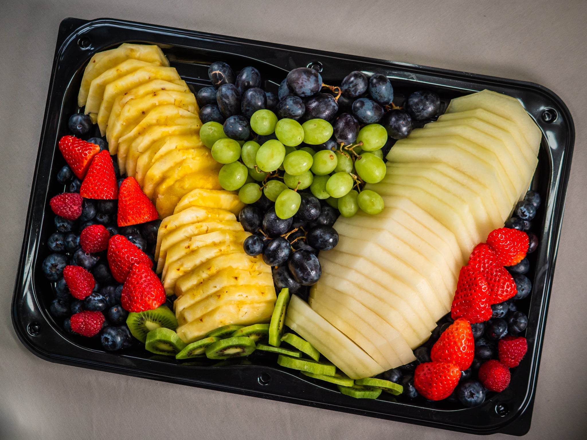 Sub Side’s Fresh Fruit Medley (serves 12/24) features sliced pineapple, carved melon, seasonal berries, and mixed grapes neatly arranged on a black tray.