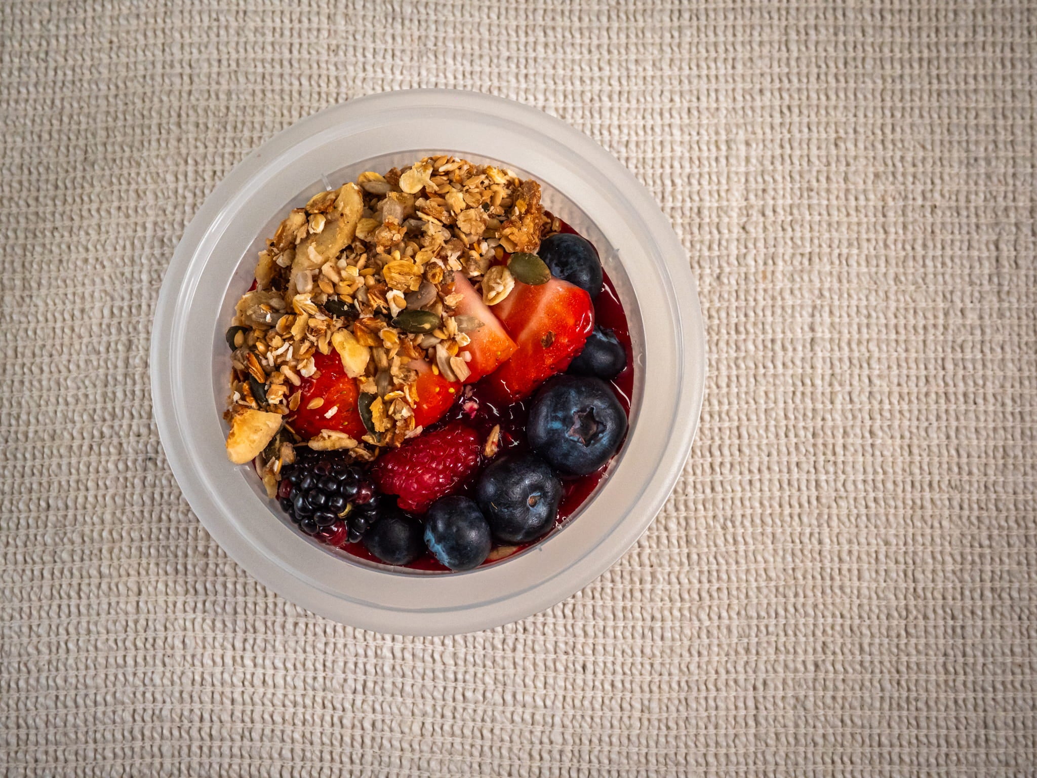 A Sub Side Yogurt Berry Snap Pot (227g) filled with granola, strawberries, raspberries, blueberries, and blackberries sits on a beige textured surface.