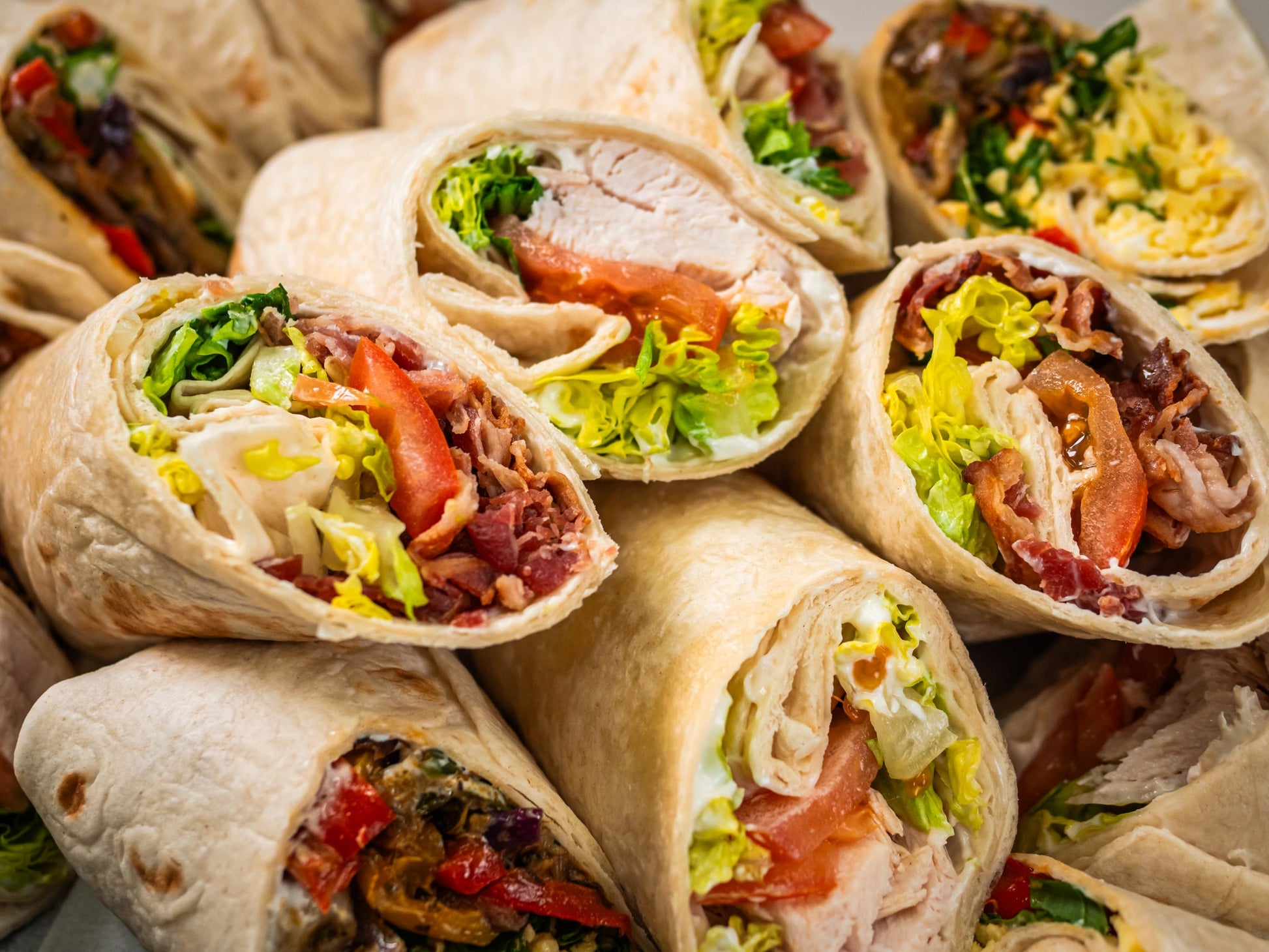 A close-up of Sub Side’s Mixed Wrap Platter—1 platter (serves 7 pax)—showcases colorful wraps packed with lettuce, tomato, deli meat, bacon, and veggies in toasted tortillas, all stacked together.
