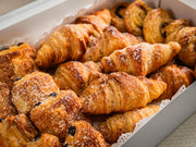 The Sub Side Assorted Mini Pastries (22 pieces) box offers a selection of golden-brown treats, including buttery croissants and pains au chocolat, some finished with powdered sugar.