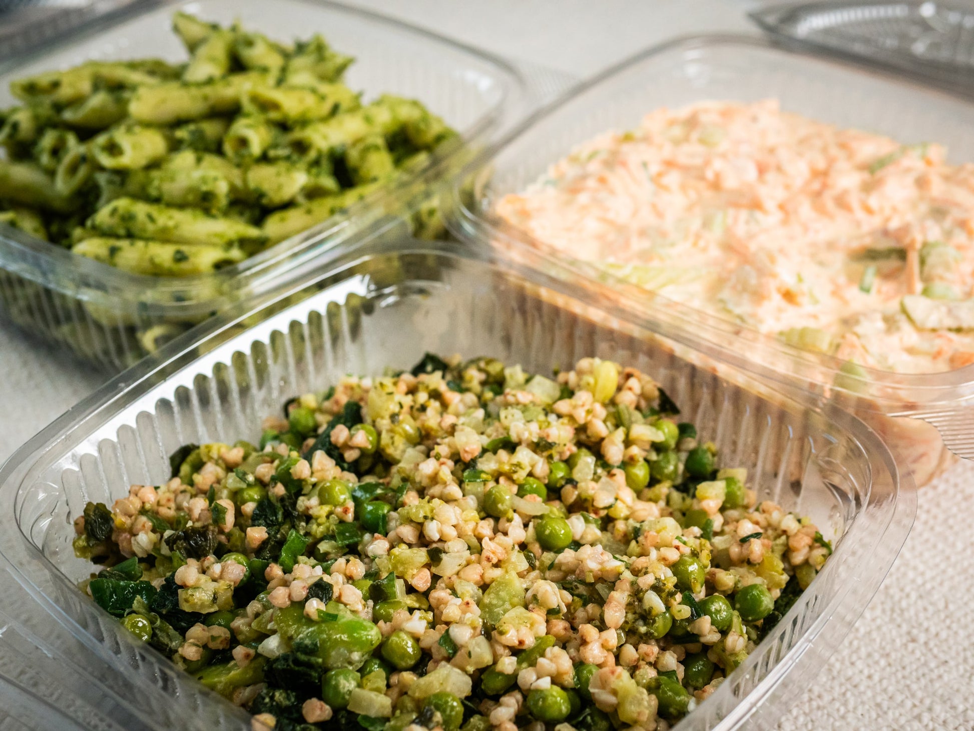 Sub Side Trio of Salads (3 x 500g) features Nut Free Pesto Pasta, Hot Honey Slaw, and a vibrant Green Wheat Salad with grains, peas, and greens, all arranged in clear plastic containers on a light surface.