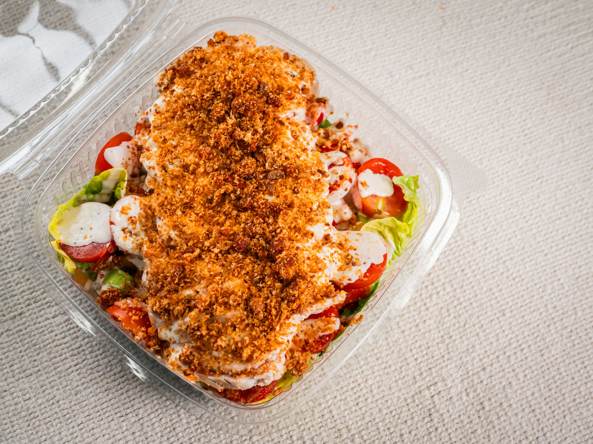 The Sub Side Sub Salad (400g) features fresh lettuce, tomatoes, cucumbers, creamy Caesar dressing, and a generous serving of breaded baked chicken in a plastic takeout container.