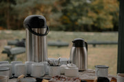 The Sub Side Tea & Coffee Service (20 pax) features large and small stainless steel coffee carafes, fresh filter coffee, white cups, sugar bowl, utensils, and pastries set outdoors with blurred trees in the background.